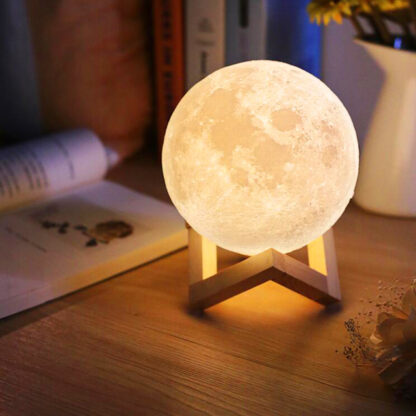 lampara de luna recargable 3d sobre mesa de madera y libro abierto al costado la luna esta encendida